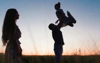 Parents playing with their daughter in a field at sunset - saving for children with Trump Accounts, 529 plans, and UTMAs