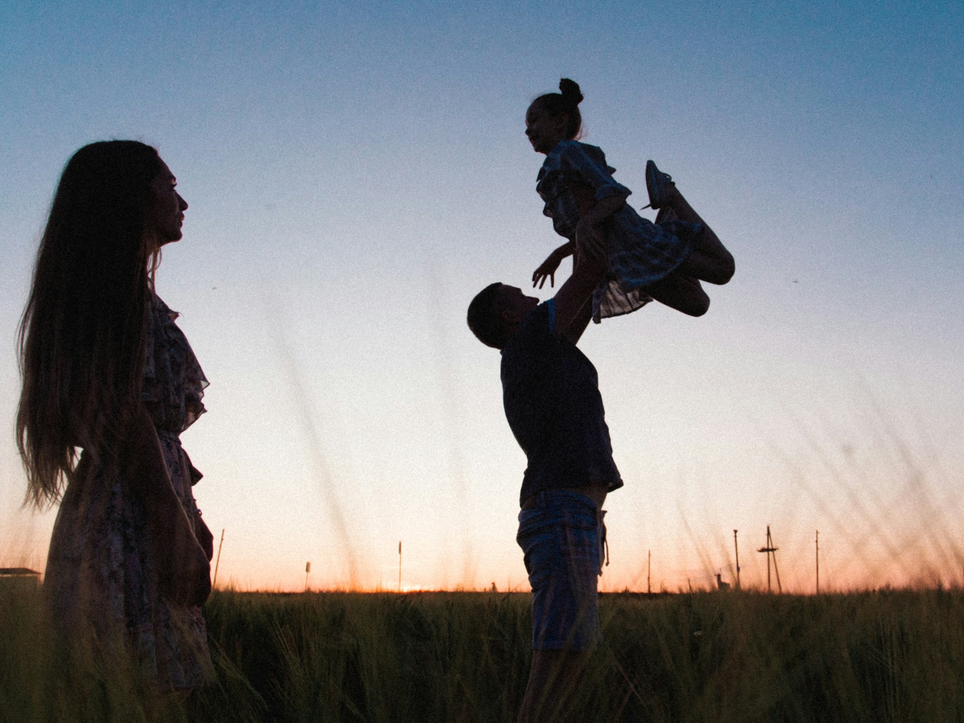 Family in field at sunset – Trump Accounts 529 UTMA guide Parents playing with their daughter in a field at sunset - saving for children with Trump Accounts, 529 plans, and UTMAs